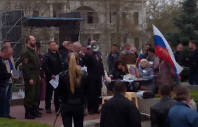 У постамента стоит стол, а на нём портрет Путина, прям как икона, светлым ликом к народу. Камера в телефоне, естественно, так себе. Поэтому кадрированное фото с высокой зернистостью. Но суть понятна. Портрет на возвышении, а присутствующие его лицезреют.